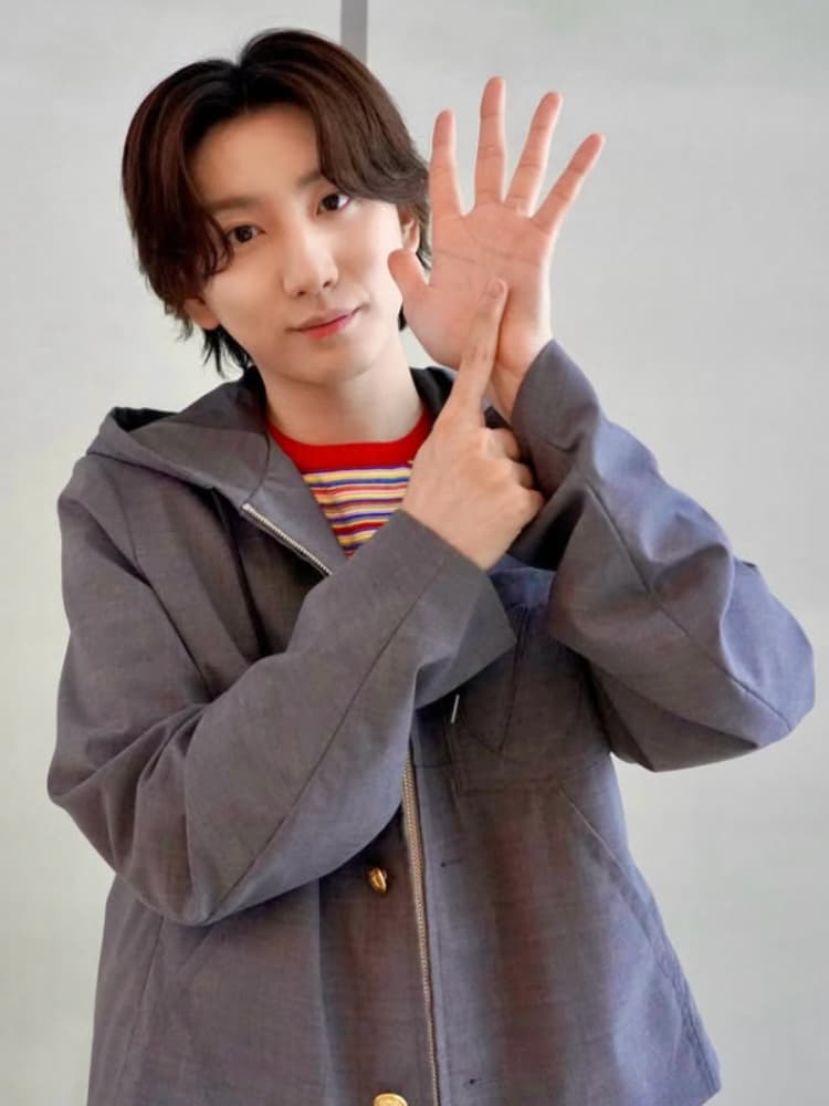 グレーのパーカーとカラフルなストライプのTシャツを着用した京本大我。右手のひらを外に向けて「5」を示し、左手の人差し指でその中心を指差している。白い背景。