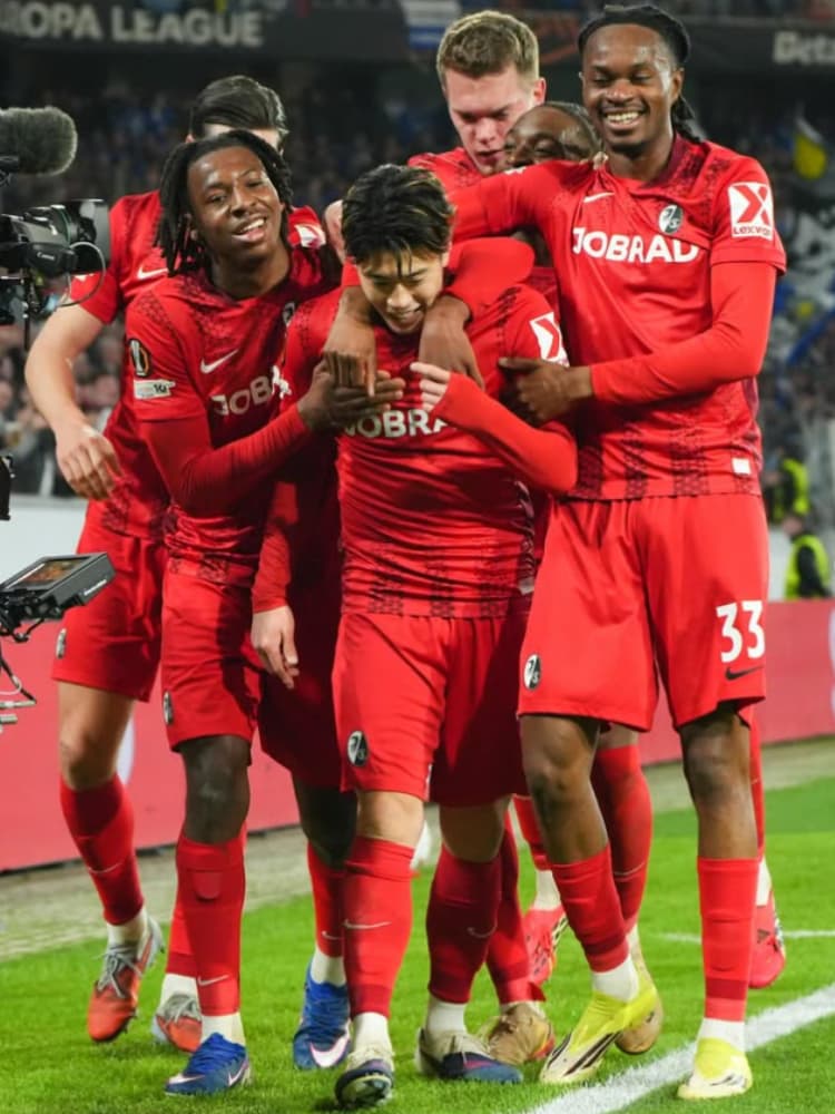 ゴール後、赤いユニフォームを着たSCフライブルクのチームメイトたちに囲まれ、手厚い祝福を受ける中心の鈴木唯人選手。