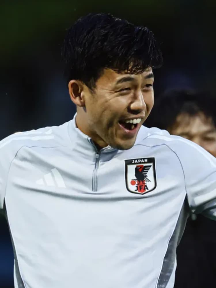 薄いグレーの日本代表トレーニングウェアを着用し、練習中あるいは試合前後のリラックスした場面で、口を開けて楽しそうに笑う遠藤航選手。