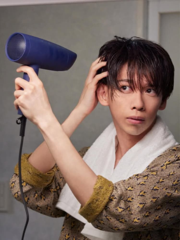 濡れた髪に白いタオルをかけ、柄物のローブを着た船津稜雅が、青いヘアドライヤーで髪を乾かしている様子。視線は斜め上を向いている