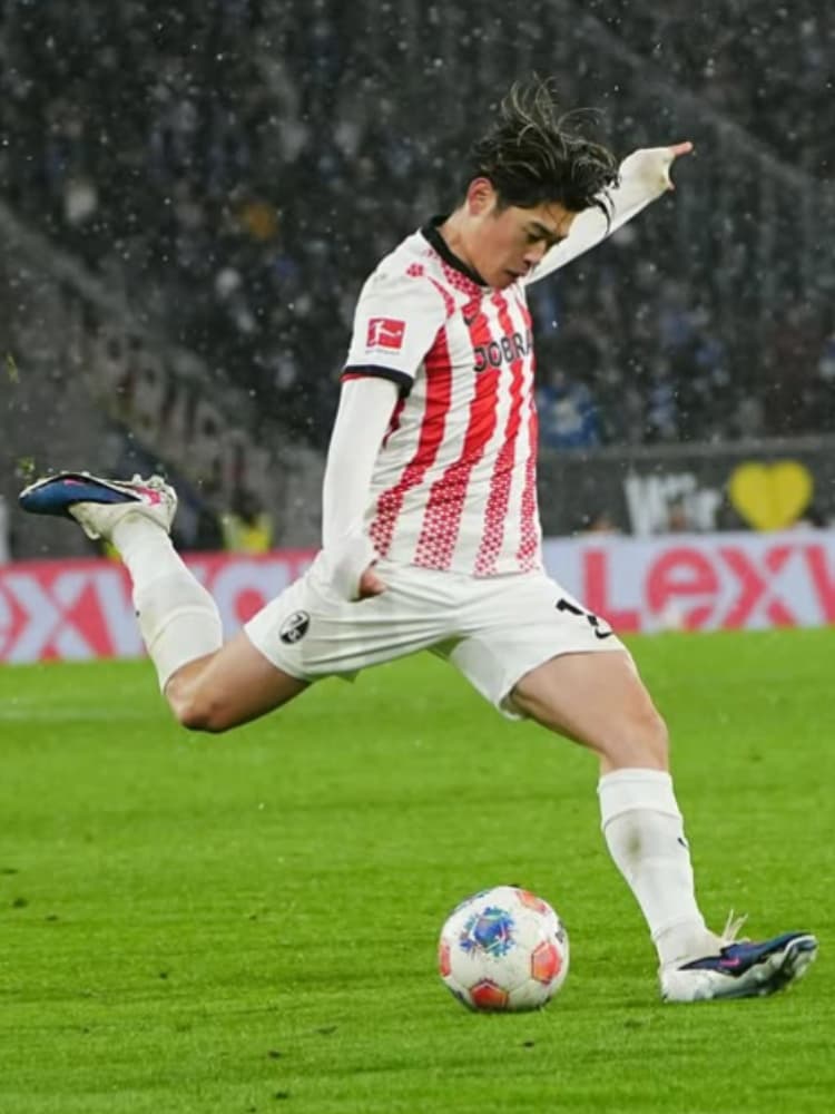 雨が降るピッチで、全身のバネを使って力強くシュートを放つ鈴木唯人選手。軸足の踏み込みからキックの瞬間までの高い技術が伝わる一枚。