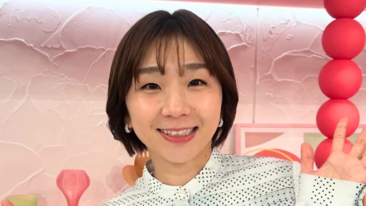 白いドット柄のブラウスを着用し、ピンク色のスタジオセットの前で笑顔で手を振る高橋成美さんのアップ写真。