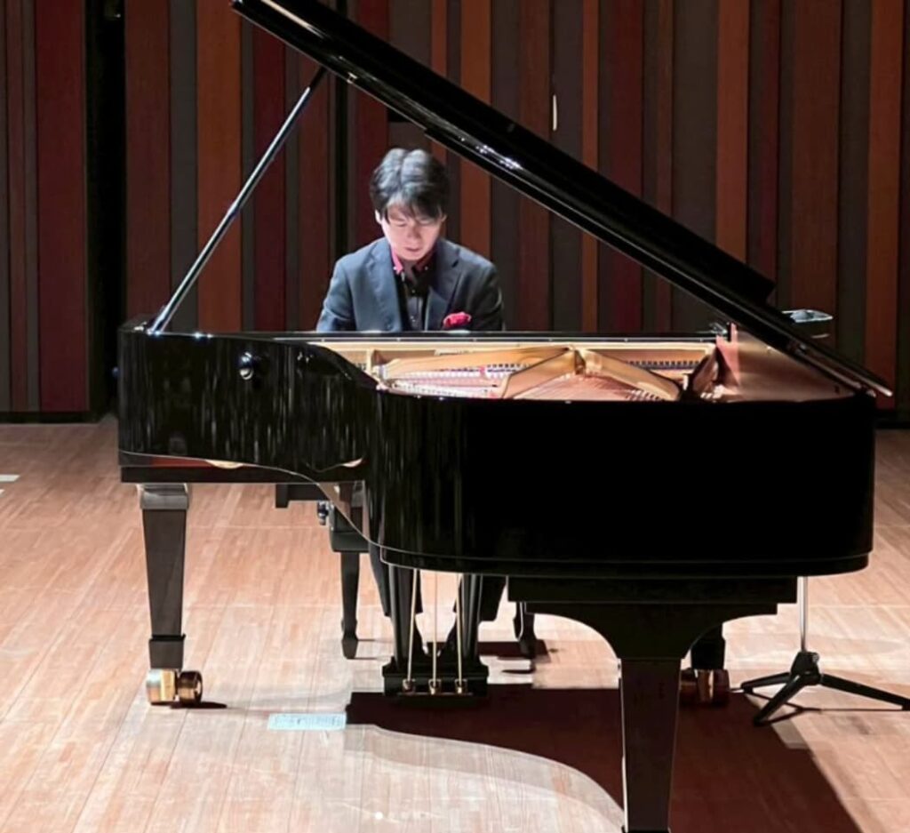 コンサートホールのステージで、グランドピアノを演奏するピアニストの福間洸太朗。
