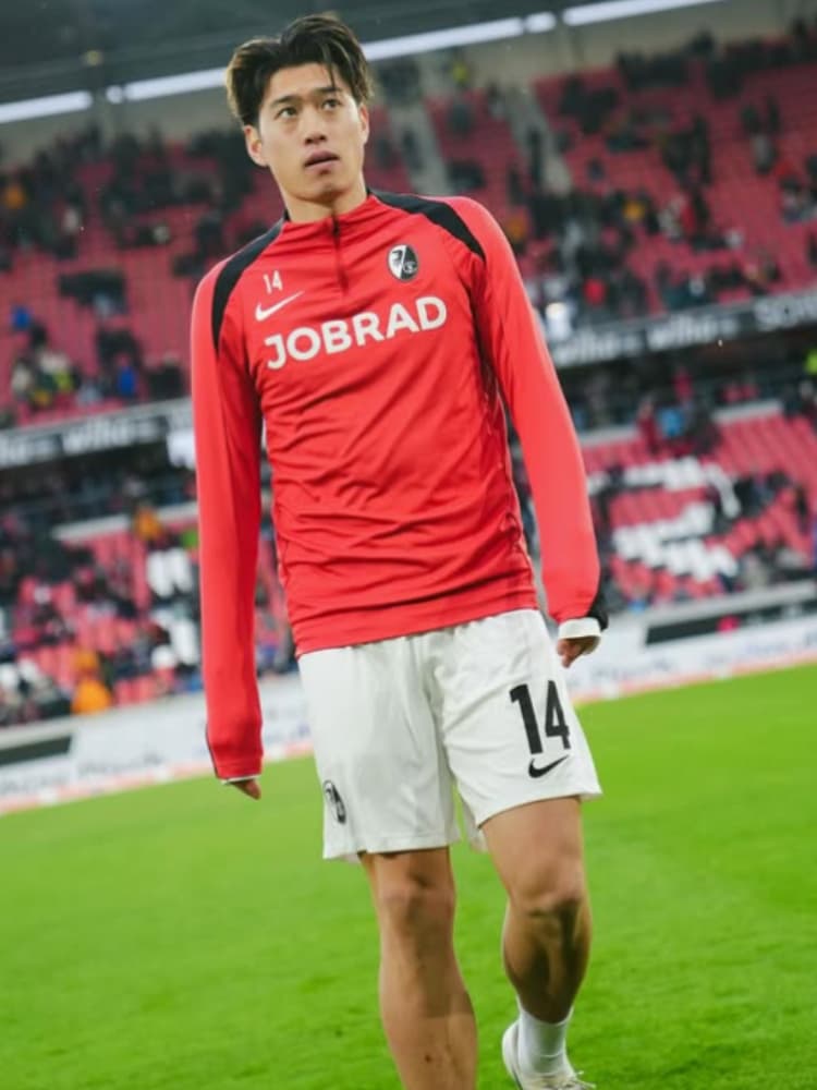 SCフライブルクの赤い長袖トレーニングウェアを着用し、ピッチ上に佇む鈴木唯人選手。パンツの背番号14が確認できる。