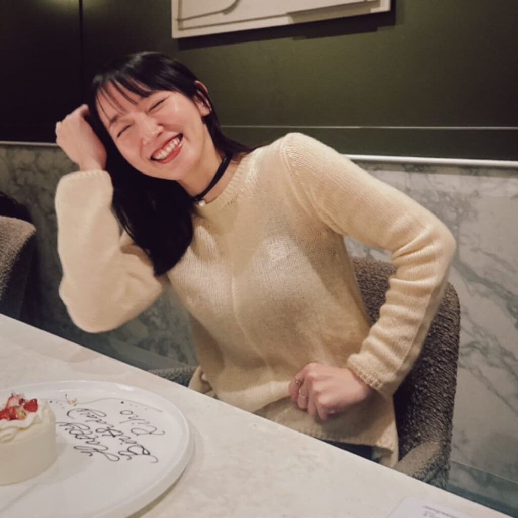 誕生日ケーキを前に、目をつぶって嬉しそうに爆笑する女優の吉岡里帆。アイボリーのニットを着用。