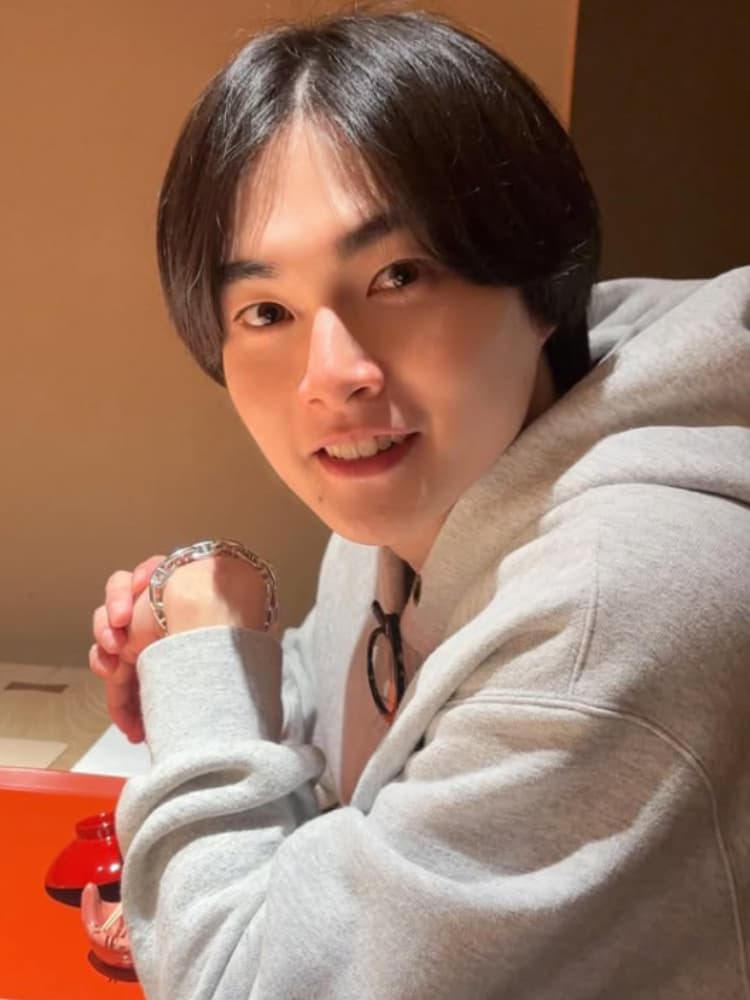 レストランでカメラ目線で座る俳優の結木滉星氏。グレーのパーカーを着ており、手元にブレスレット。